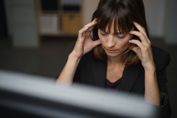 Businesswoman suffering from a headache or migraine holding her hands to her throbbing temples as she works late in the office to a deadline.jpeg